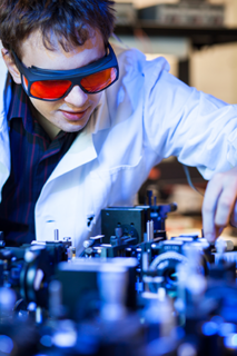 The image shows a young male scientist in a laser lab.